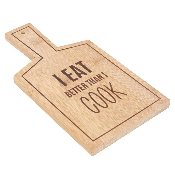 Wooden cutting board with 'I eat better than I cook' text on a white background