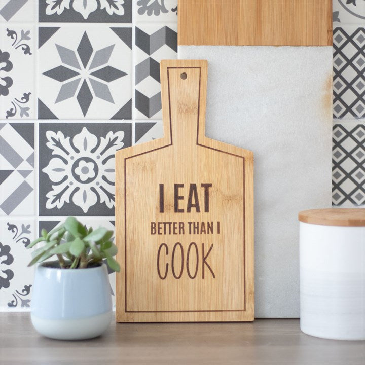 Wooden cutting board with 'I Eat Better Than I Cook' text on a kitchen counter.